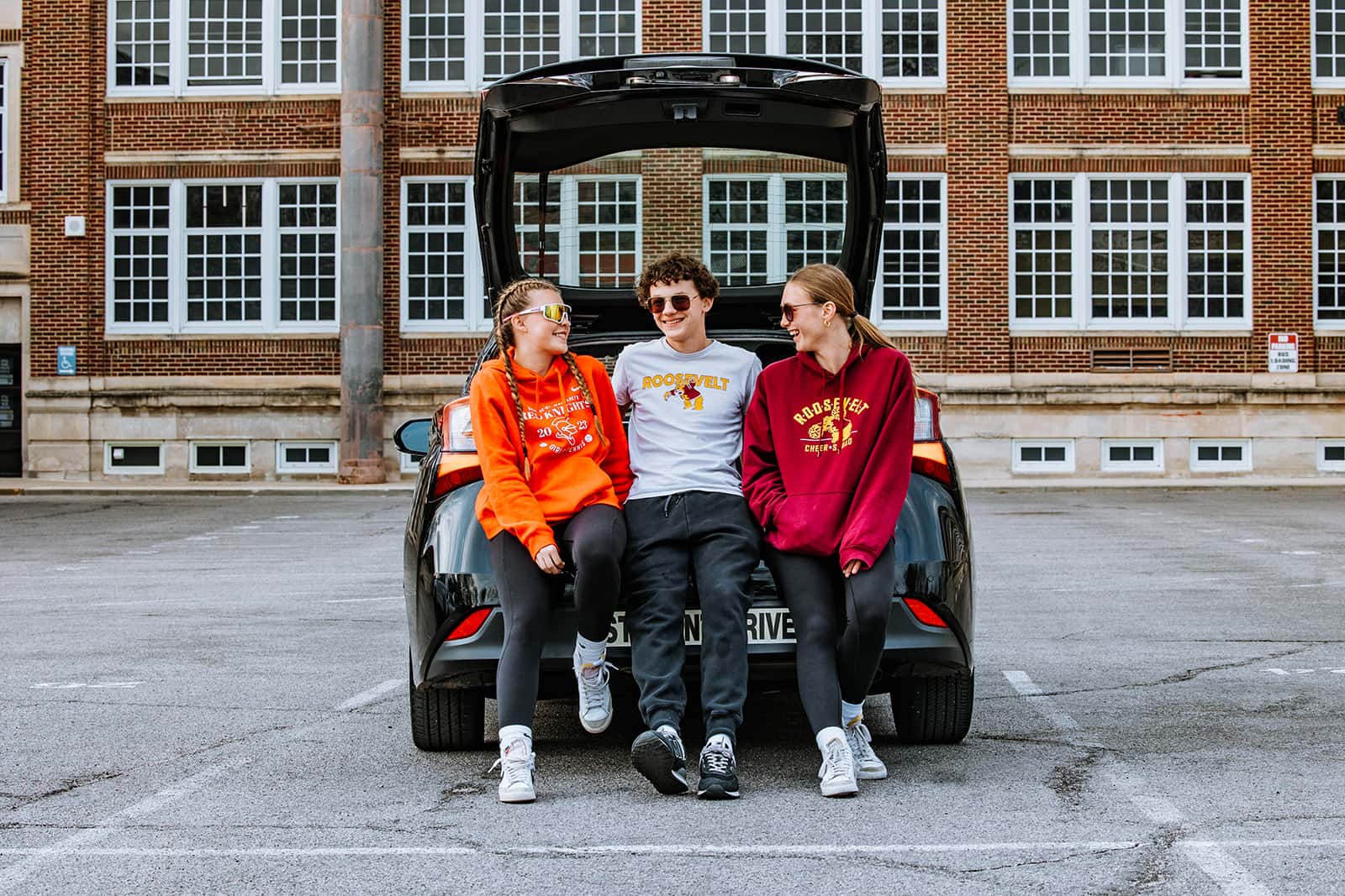 Group of ten high school driver's education students standing together in parking lot wearing college sweatshirts